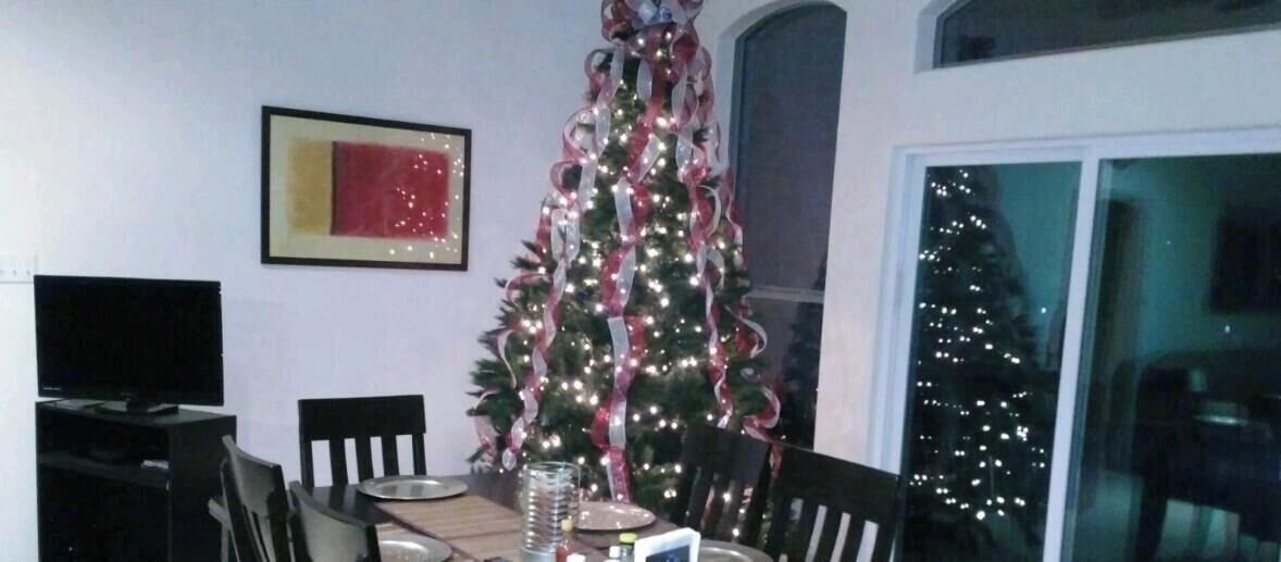 A dining area with a Christmas tree, a framed picture on the wall, and a window with a view of a building.