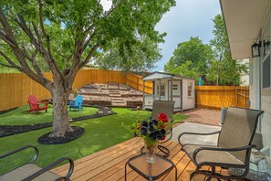 Un patio trasero con una terraza de madera, un árbol, un cobertizo pequeño y un área de patio con sillas y una mesa.