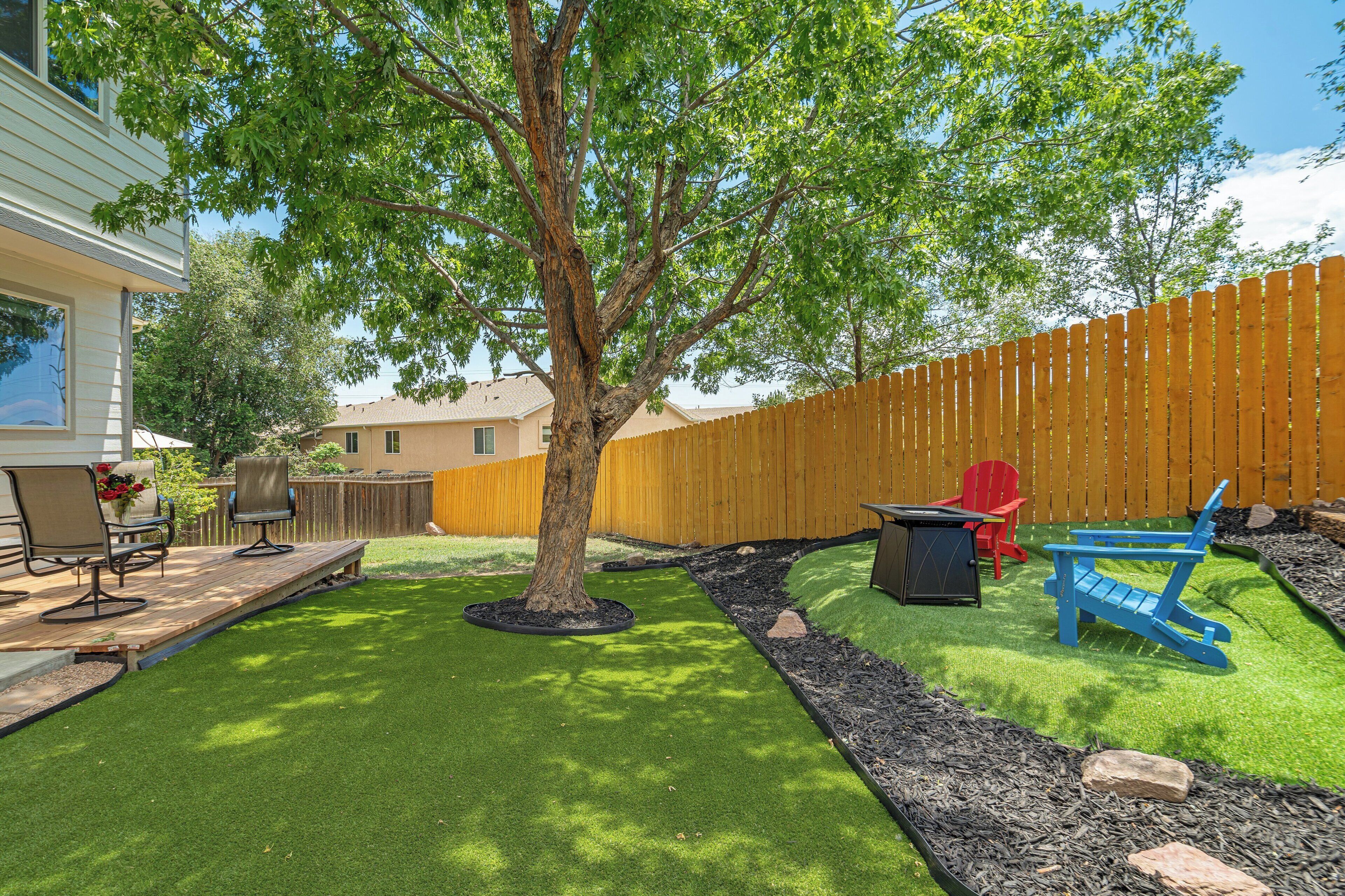 Ein Garten mit Baum, Kunstgrashalm, Holzterrasse und Gartenmöbeln.