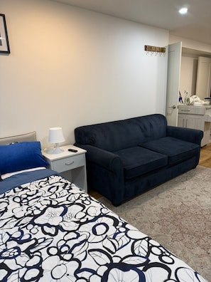 A bedroom with a bed, a dark blue sofa, a nightstand, a lamp, and a door leading to a bathroom. - Private beautiful Suite in Bungalow (Brossard)