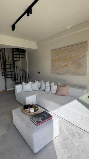 Ein modernes Wohnzimmer mit einer Eckcouch, einem Couchtisch mit einem Buch, einer Wanddekoration und einer Wendeltreppe.