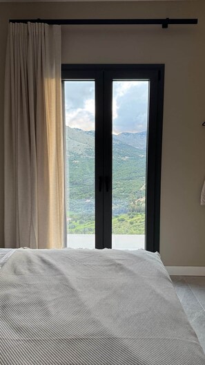 Ein Schlafzimmer mit einem großen Bett und einer Schiebetür zu einem Balkon mit Bergblick.