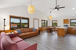 Ein modernes Interieur mit Sofa, Essbereich, Küche und großen Fenstern.