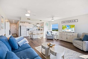Ein modernes Wohnzimmer mit einer Couch, einem Fernseher und Blick auf den Strand.