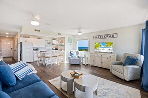Ein modernes Wohnzimmer mit einem blauen Sofa, einem gemusterten Sessel und einem Essbereich mit weißen Stühlen.