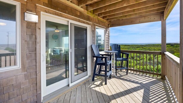 Une terrasse en bois avec une porte vitrée donnant sur une pièce, un espace salon extérieur et une vue sur le paysage.