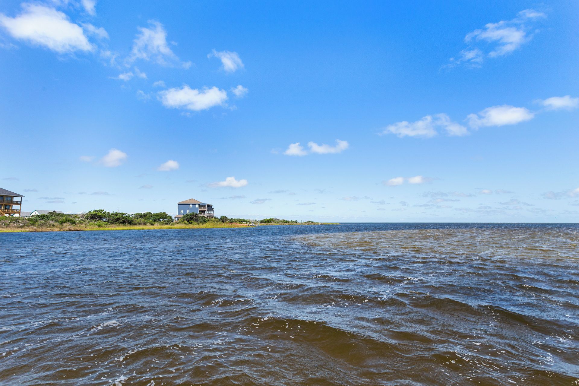 A coastal view with a house on a peninsula, a body of water, and a clear sky.