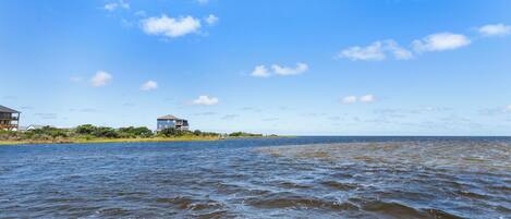 A coastal view with a house on a peninsula, a body of water, and a clear sky.