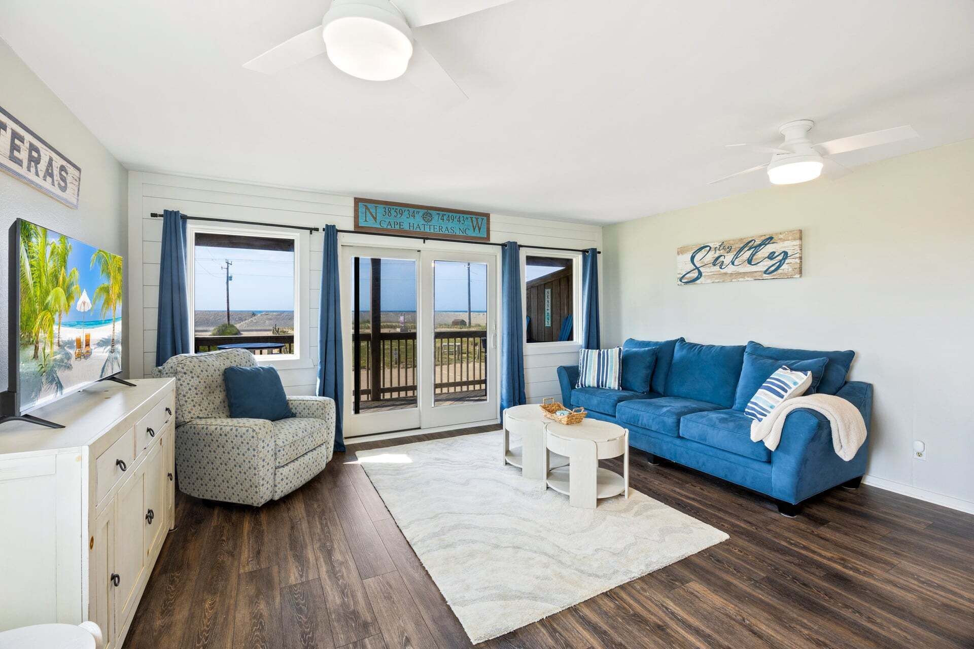 A room with a blue sofa, a patterned armchair, a TV, and a sign indicating Cape Hatteras, NC.