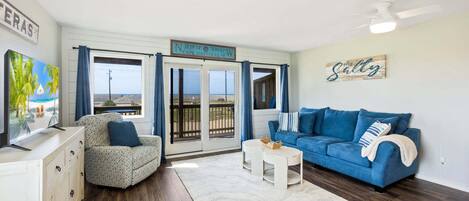 A room with a blue sofa, a patterned armchair, a TV, and a sign indicating Cape Hatteras, NC.