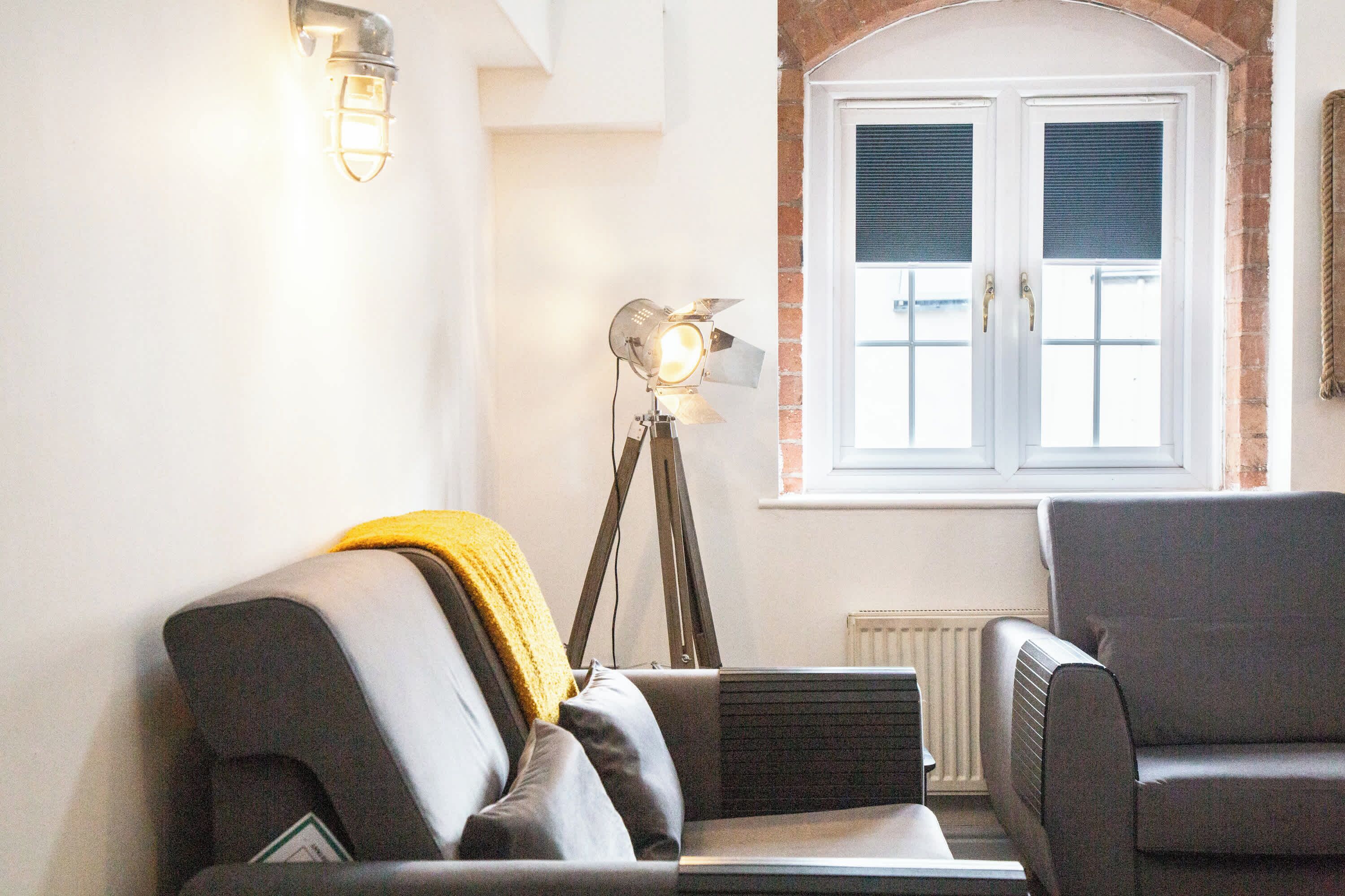 A living room with a sofa, armchair, floor lamp, and a window with shutters.