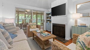 A living room with a sofa set, a coffee table, a fireplace, a television, and a view of the outdoors. - 3BR golf-course cottage on Seabrook Island w/screened porch "Serene Seahorse"-no pets (Seabrook Island)