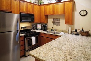 A kitchen with wooden cabinets, stainless steel appliances, granite countertops, a clock, and a decorative wall piece. - La Quinta Desert Escape · Pools, Golf, Old Town (La Quinta)