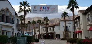 Un carrer amb edificis, palmeres i un banner publicitari d'un esdeveniment.