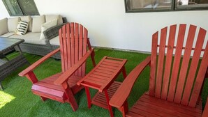 A patio with a red Adirondack chair, a matching bench, and a small table.