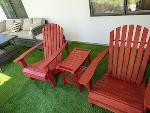 Eine Terrasse mit einem roten Adirondack-Stuhl, einer passenden Bank und einem kleinen Tisch.