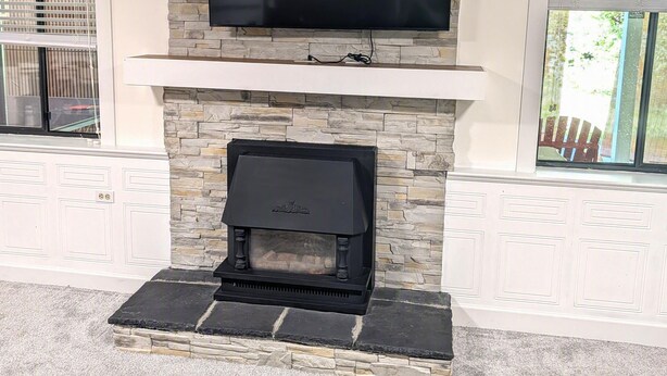 A fireplace with a stone surround, a mounted television above it, and a view of the outdoors through a window.