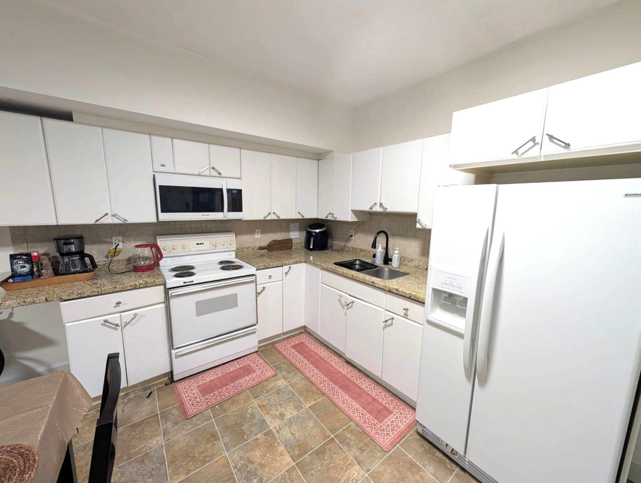 A kitchen with white cabinets, a microwave, stove, sink, and a refrigerator.