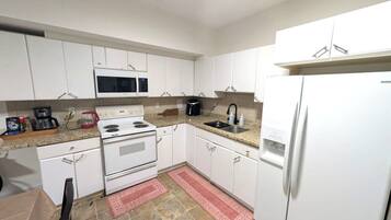A kitchen with white cabinets, a microwave, stove, sink, and a refrigerator.