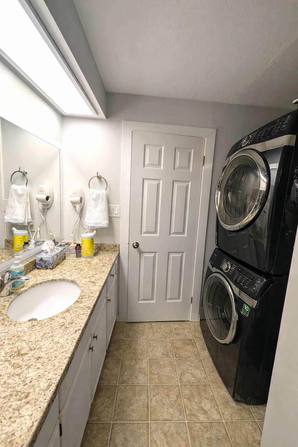 A compact laundry room with a sink, towel rack, and a front-loading washer and dryer.