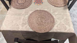 A square table with a woven placemat, a decorative coaster, and a woven placemat on the tablecloth.