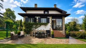 Een huis met twee verdiepingen, een stenen gevel, een terras met buitenmeubilair en uitzicht op de groene omgeving.