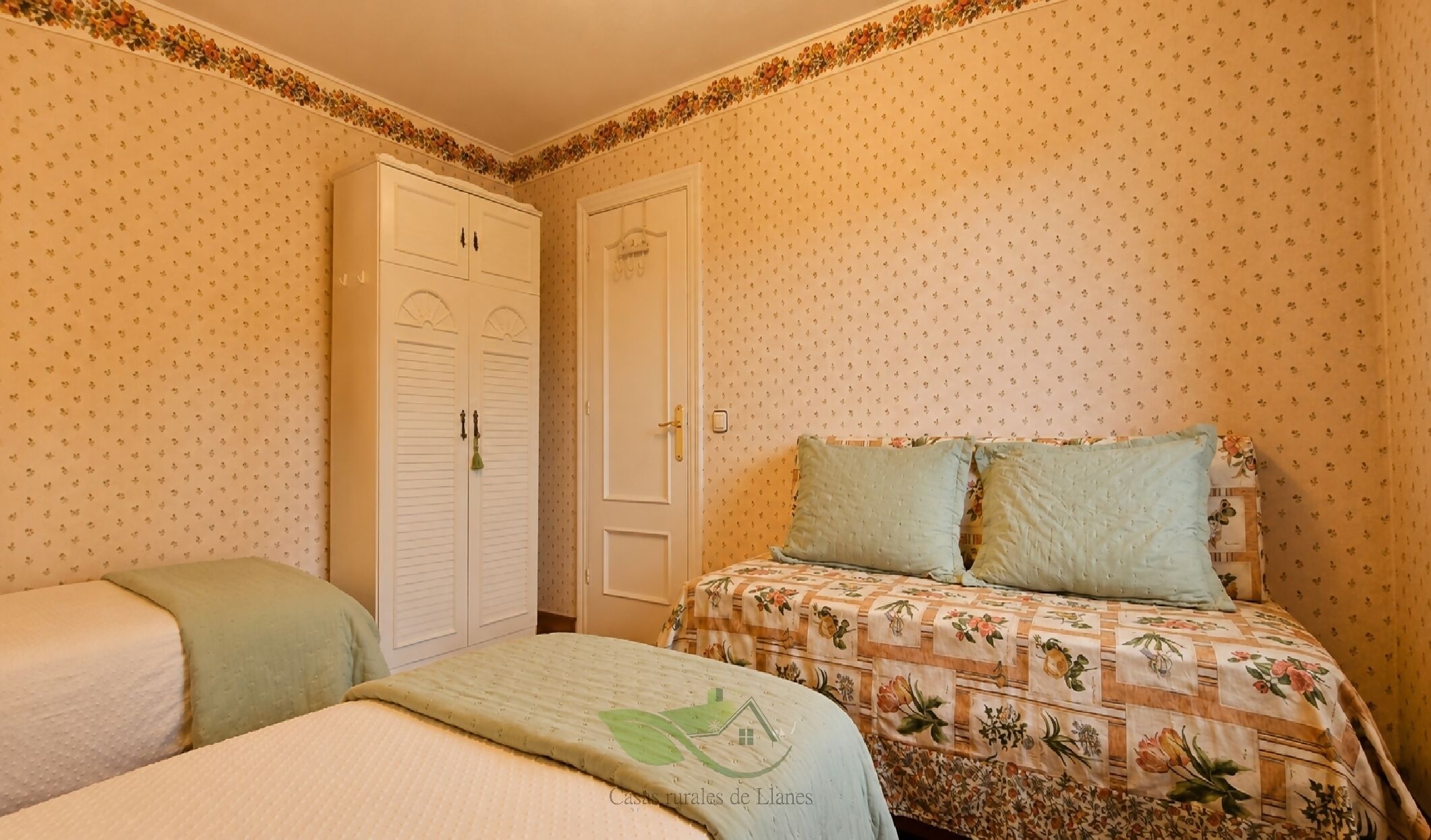 Un dormitorio con una cama, dos mesitas de noche, un armario y papel tapiz estampado con motivos florales.
