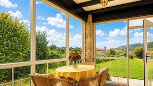 Een oranjerie met een tafel en stoelen, een bloevas en uitzicht op een groen landschap.