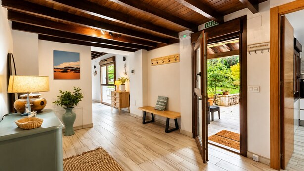 Um corredor com piso de madeira, um banco, uma luminária, um vaso com uma planta, um quadro na parede e uma porta que dá para uma área externa.