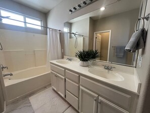 Ein Badezimmer mit einer Badewanne, zwei Waschbecken, einem großen Spiegel und einer Zimmerpflanze.