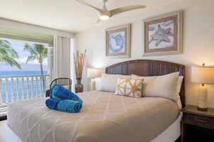Habitación de hotel con cama, vista al océano, ventilador de techo y obras de arte en la pared.