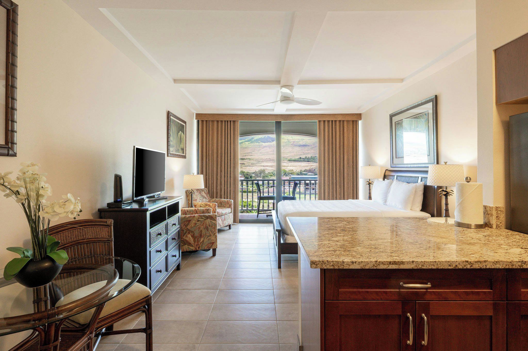 A hotel room with a balcony, a TV, a dining area, and a bed.