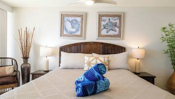 A neatly made bed with a rolled towel, two wall-mounted lamps, a wooden headboard, and two framed artworks above the bed.