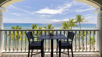 Un balcón con una mesa y sillas, con vista a una playa con palmeras y el océano.