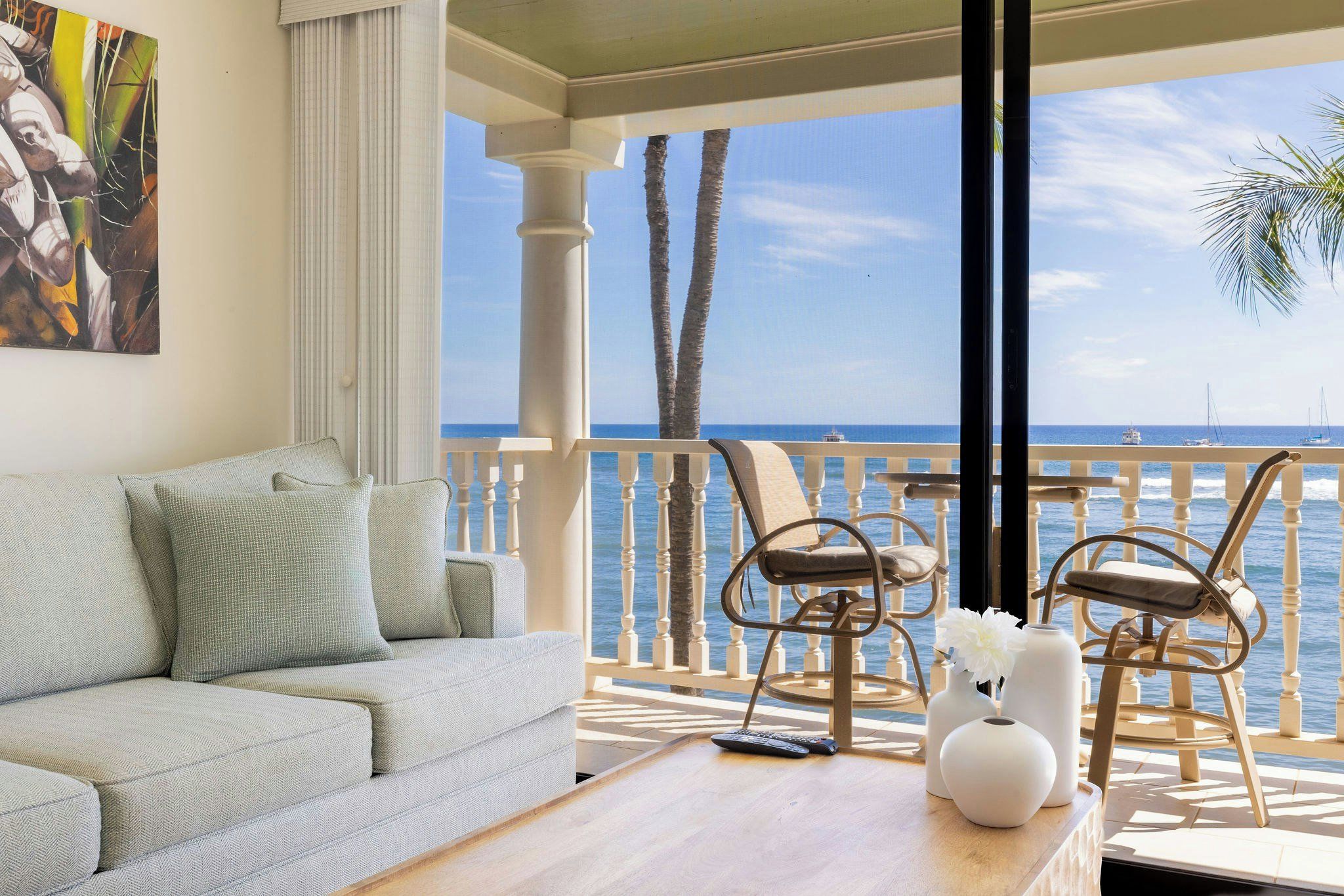 Un balcon avec vue sur la mer, un canapé, deux fauteuils et une table avec un vase et une télécommande.