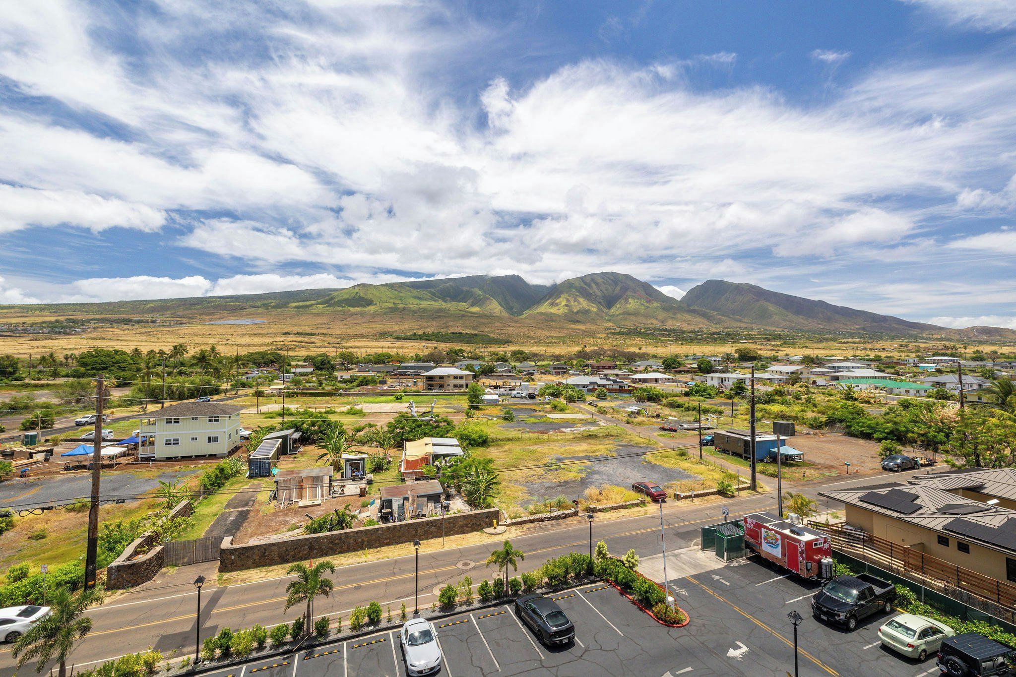 A parking lot with several cars, a building with a flat roof, and a mountainous landscape in the background.