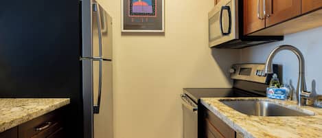 A compact kitchen with a refrigerator, microwave, stove, sink, and cabinets.