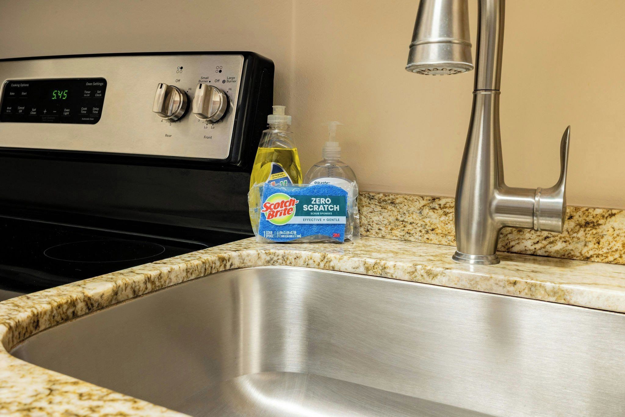 A stainless steel kitchen sink with a granite countertop, a stove with oven settings, and a faucet.