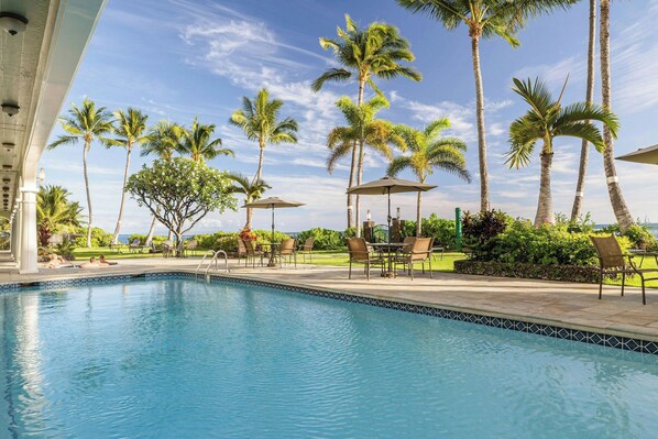 A pool area with lounge chairs and umbrellas, surrounded by palm trees and a clear sky. - Lahaina Shores Beach Resort By Castle  (Lahaina)