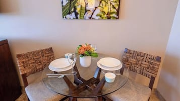 A round glass table with a woven chair backrest, a white vase with flowers, and a glass of water.