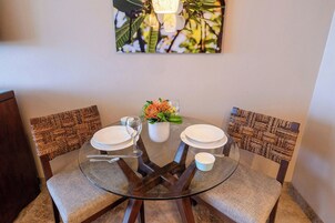 Une table ronde en verre, une chaise dont le dossier est fait d’un motif tissé, un vase blanc rempli de fleurs et un verre d’eau.