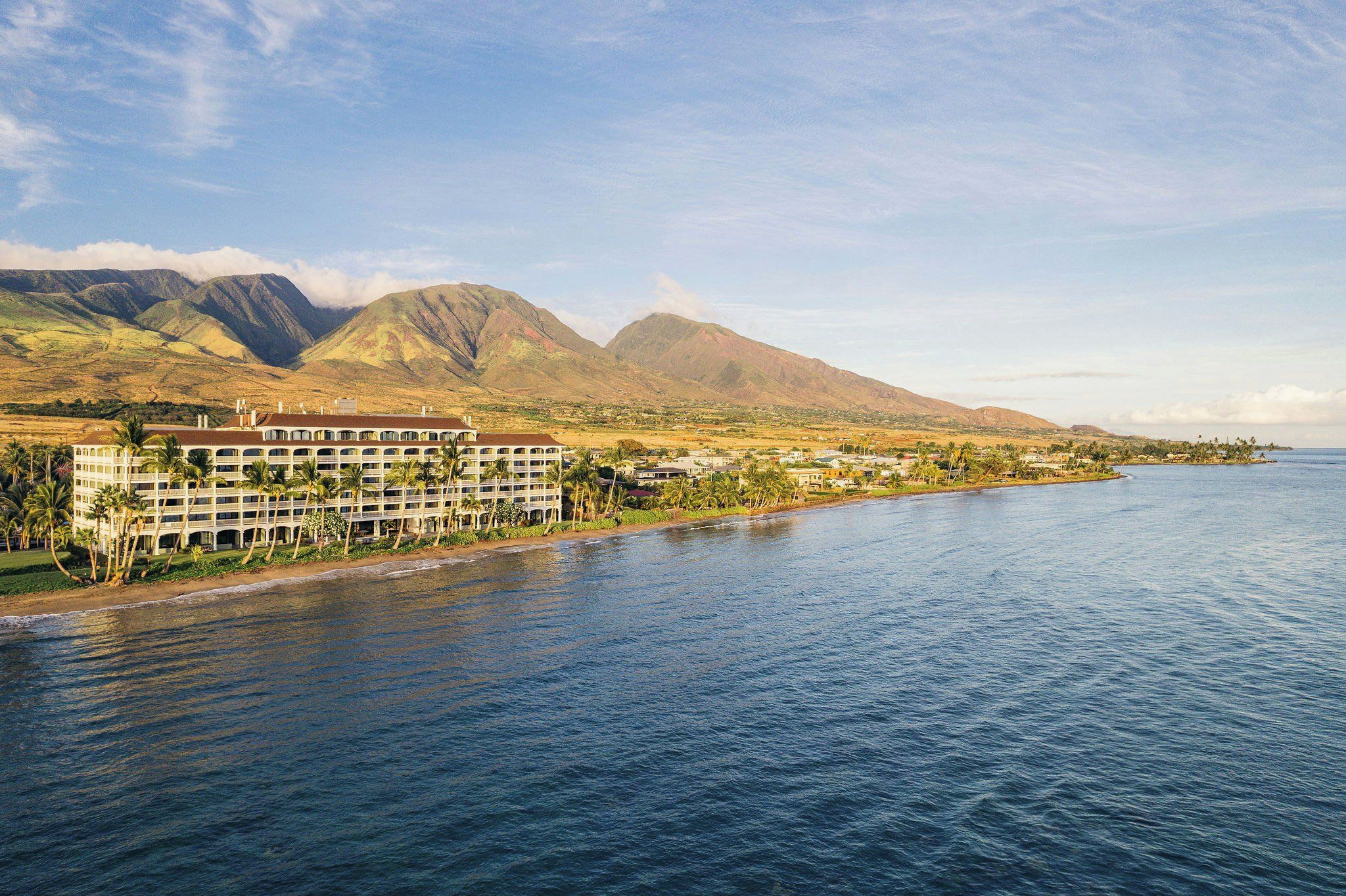 Ett hotell vid kusten med flera våningar, utsikt över stranden och berg i bakgrunden.