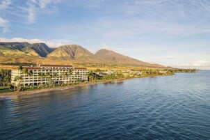 Un hotel costero con varios pisos, vista a la playa y montañas al fondo.