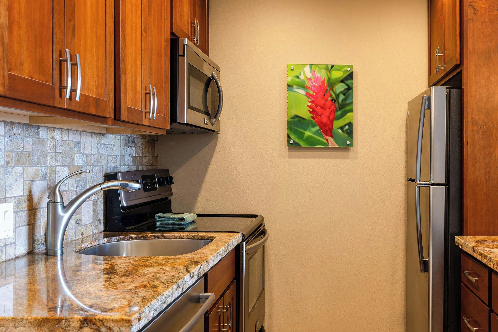 A kitchen with granite countertops, stainless steel appliances, wooden cabinets, and a wall-mounted picture of a red flower.