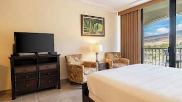 Habitación de hotel con cama, televisor en una cómoda, dos sillones, una mesa con lámpara y un amplio ventanal con vistas.