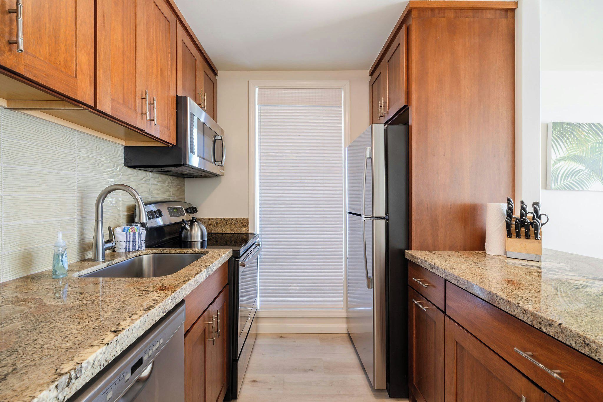 A kitchen with wooden cabinets, a stainless steel sink, a microwave, a refrigerator, and a granite countertop.
