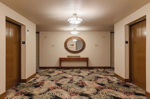 Um corredor com carpete estampado, um espelho redondo com moldura decorativa e duas portas de madeira com placas de 'SAÍDA'.