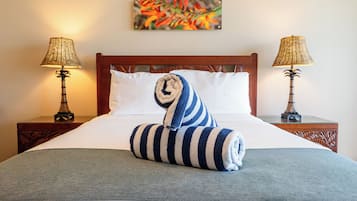 Una cama bien hecha con una toalla a rayas, dos lámparas de noche y un cuadro de colores en la pared.