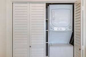 A compact laundry room with a front-loading washer and dryer, a door with a silver handle, and a white exterior.