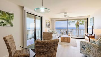 Ein geräumiges Wohnzimmer mit Balkon und Meerblick, möbliert mit Korbstühlen und einer Couch, sowie einem Deckenventilator.